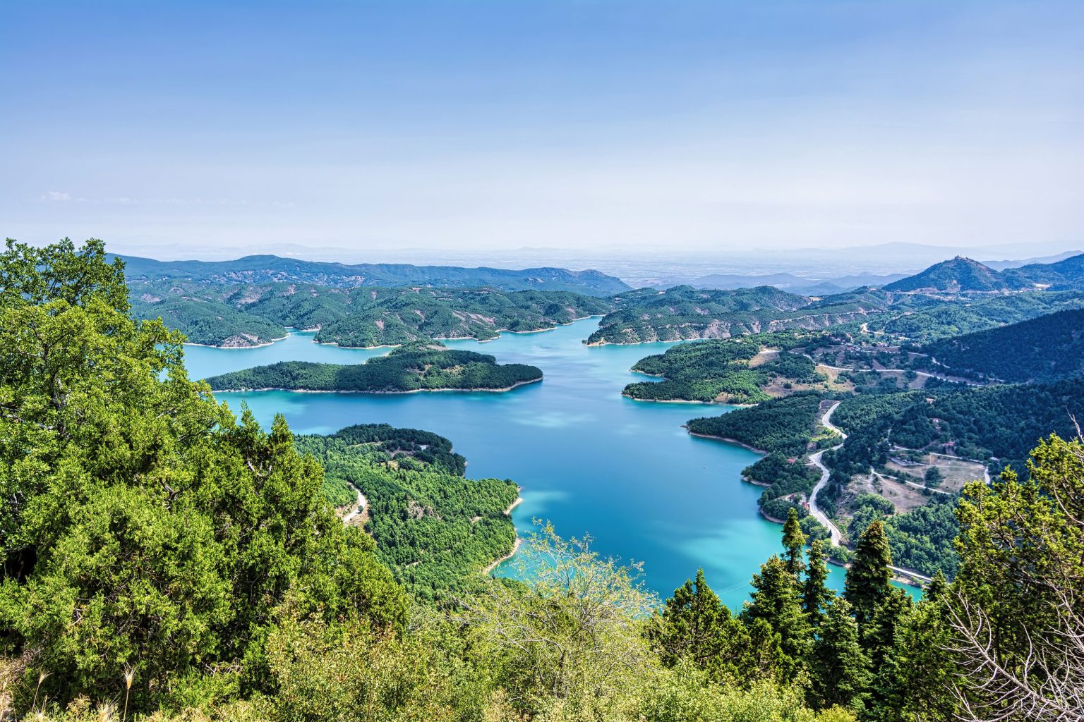 Turquoise reservoir winding between green hills in central Greece