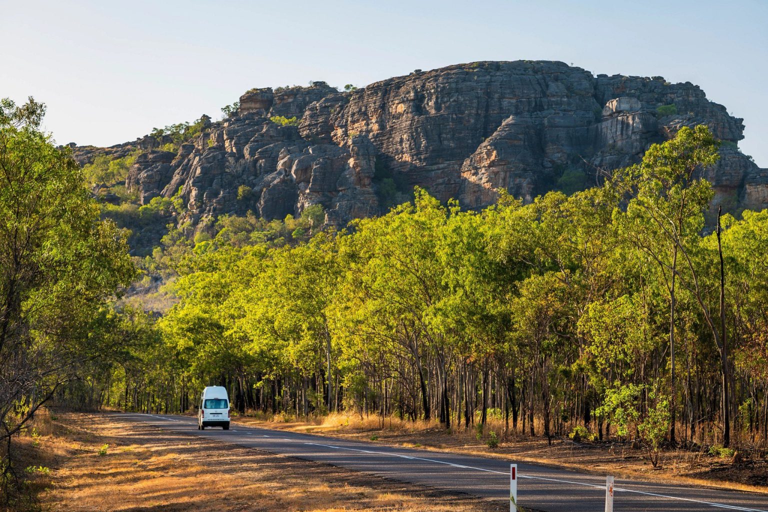 Campervan on a road below a sandstone escarpment, Kakadu National Park, the Northern Territory
