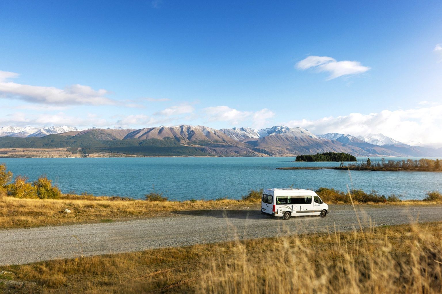 Campervan on a lakeside road below snow-capped mountains, Lake Wanaka, New Zealand's South Island