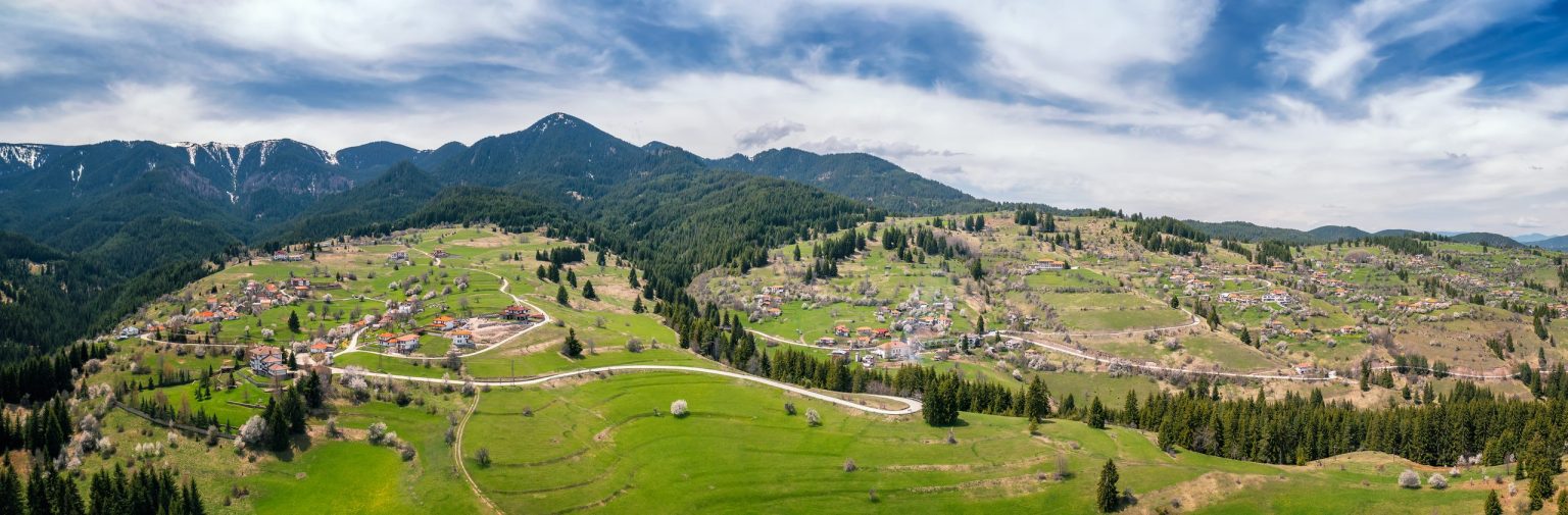 Mountain village and meadows below forested peaks in Bulgaria
