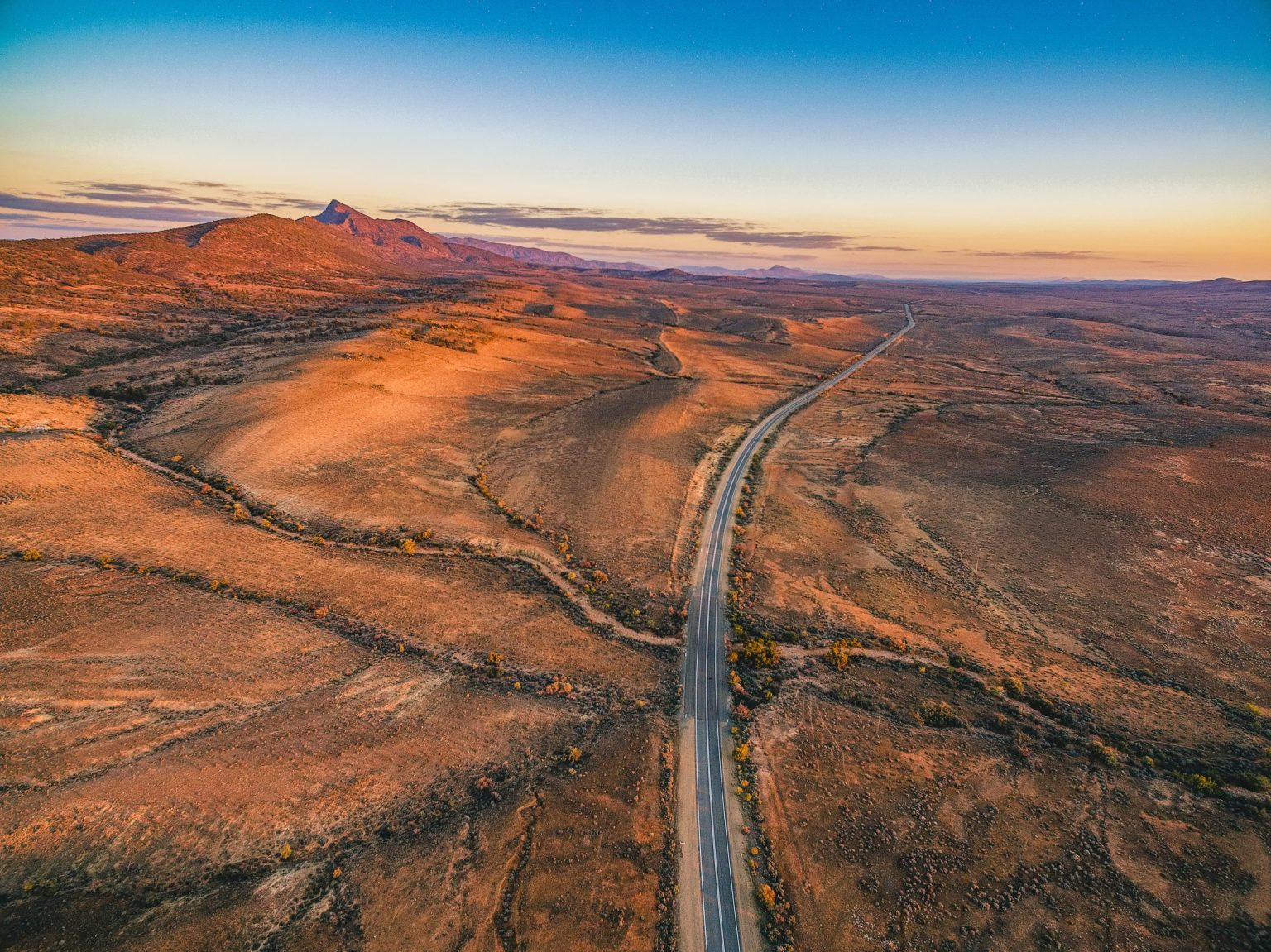 Outback road crossing red ranges at sunset