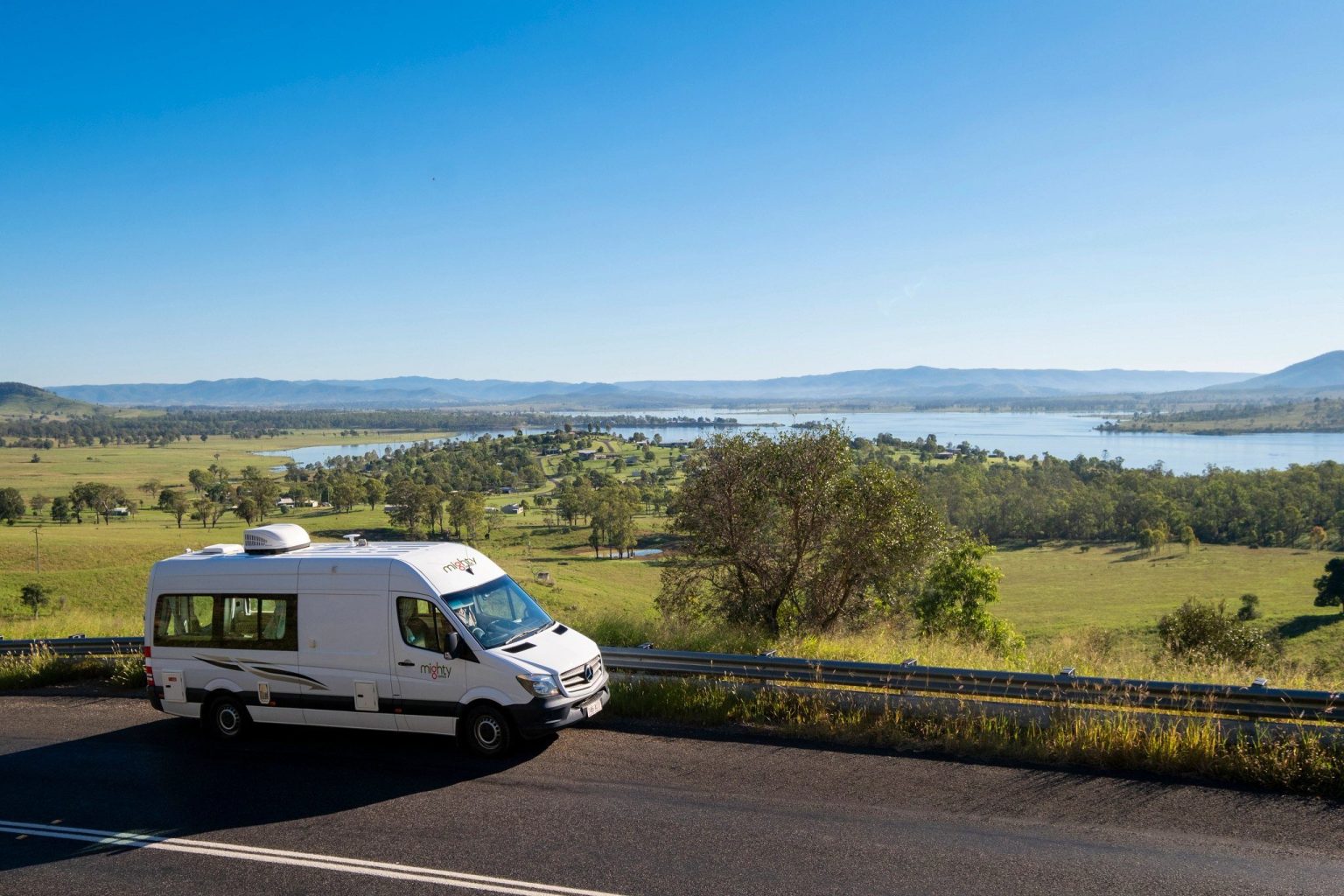 Campervan on a road above a wide valley and lake, Queensland