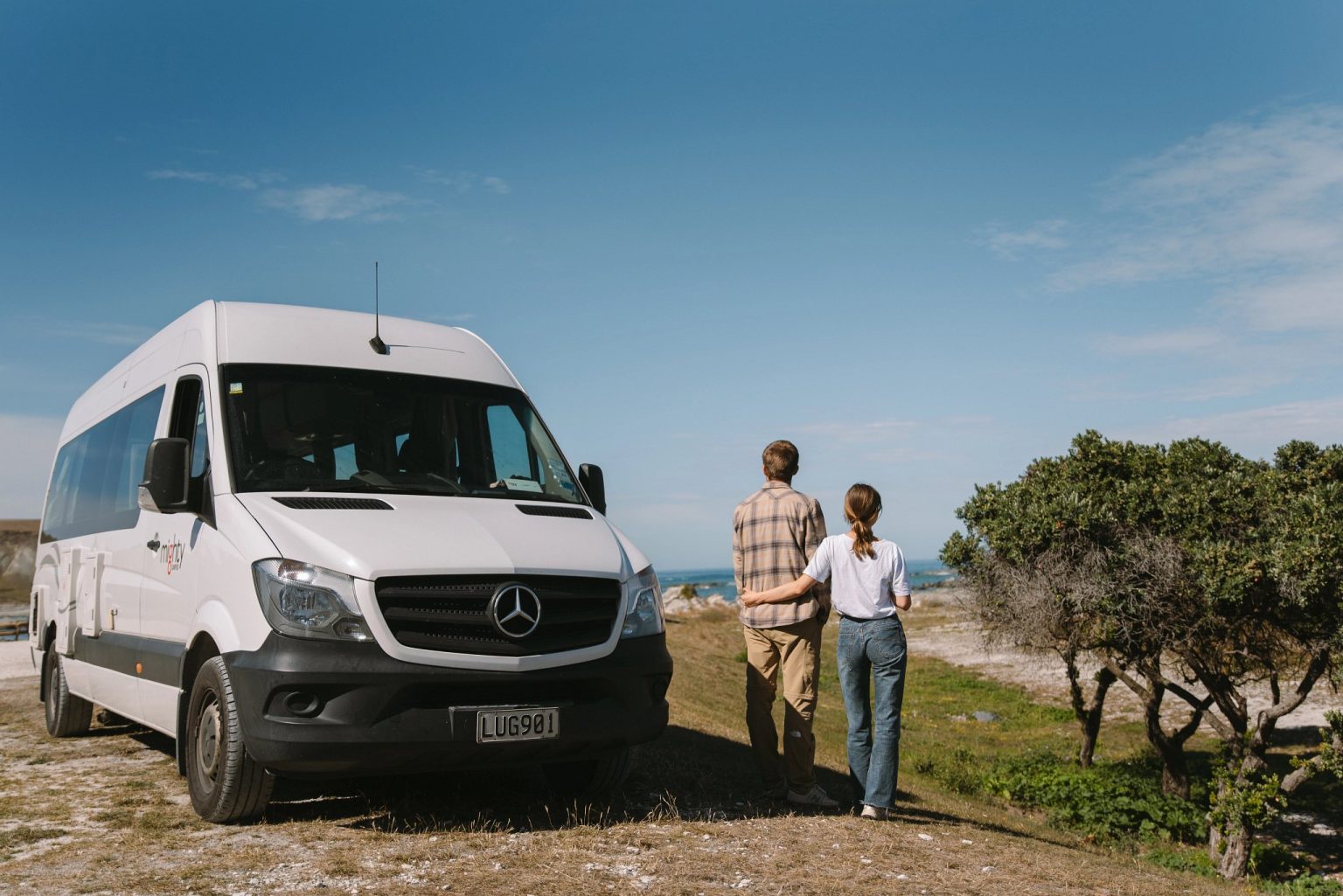 Couple standing beside a campervan on a grassy headland, Kaikoura, New Zealand's South Island