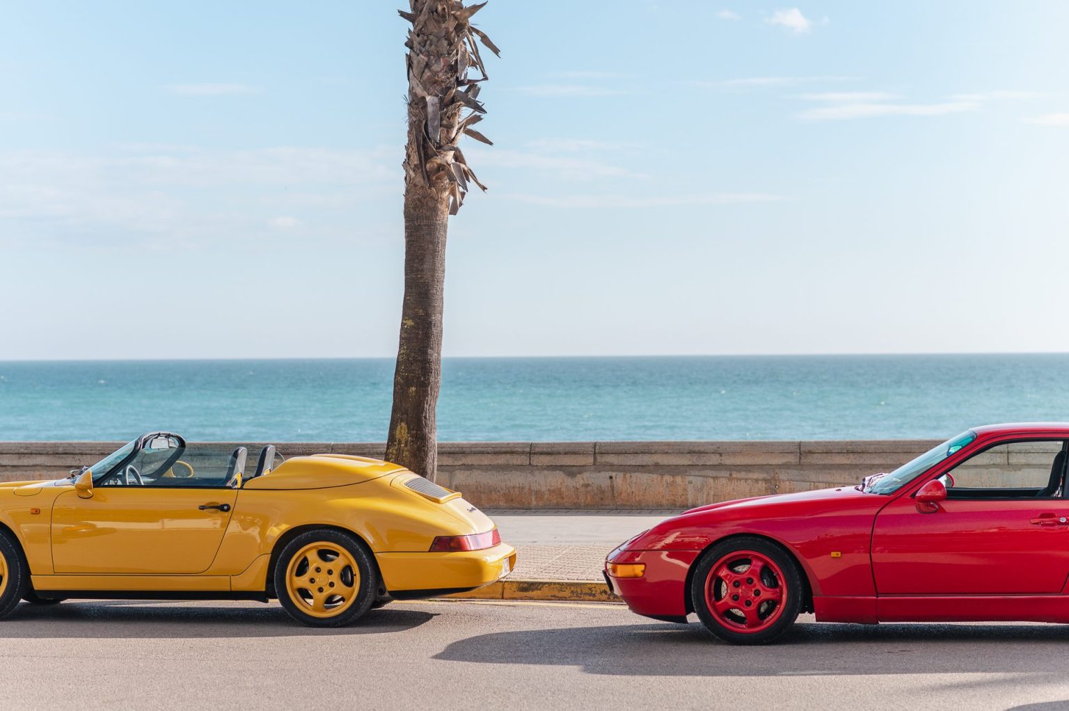 Yellow and red classic Porsches parked on a seafront promenade in Catalonia