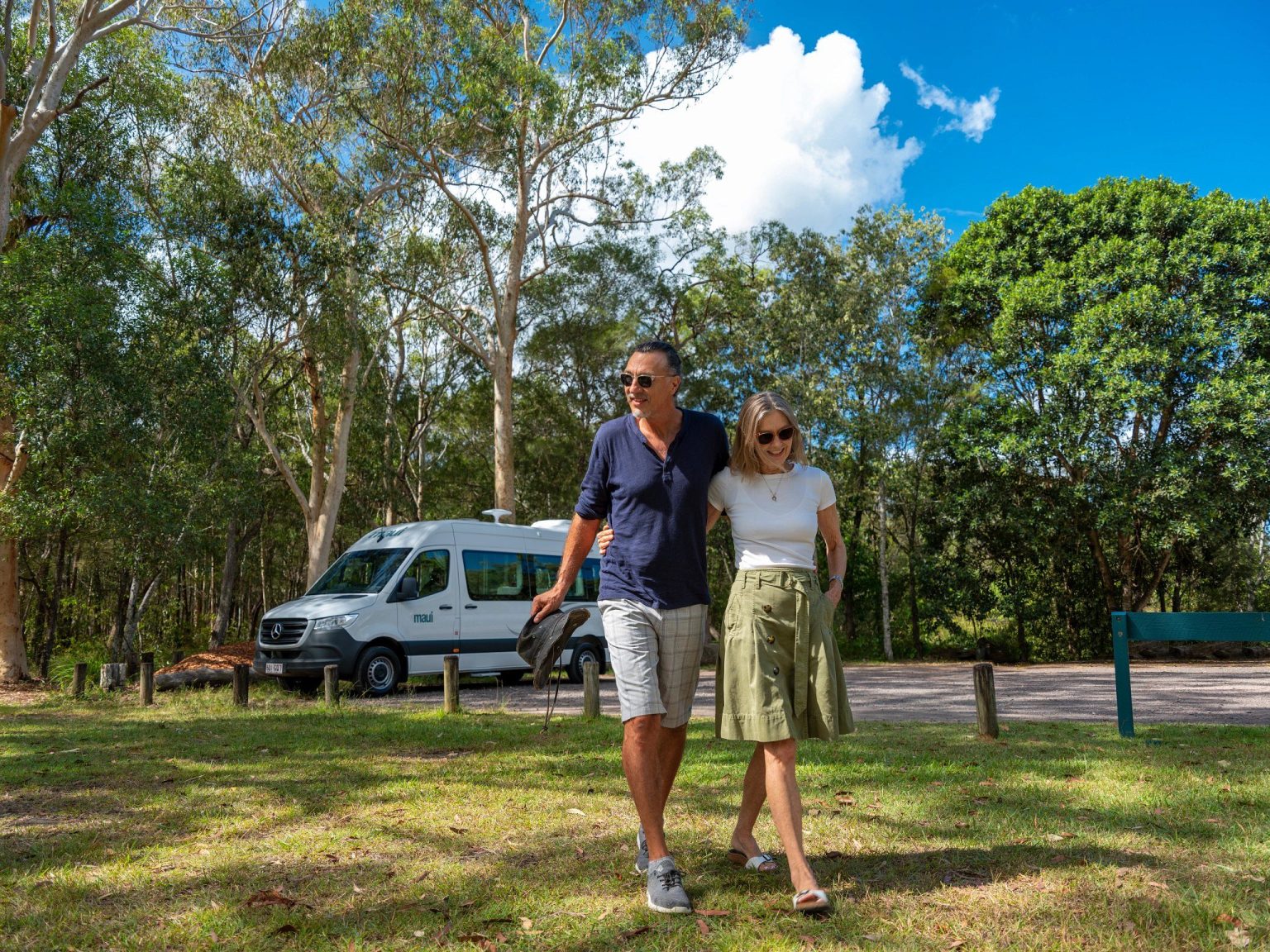 Couple strolling on grass beside a campervan in woodland, Queensland