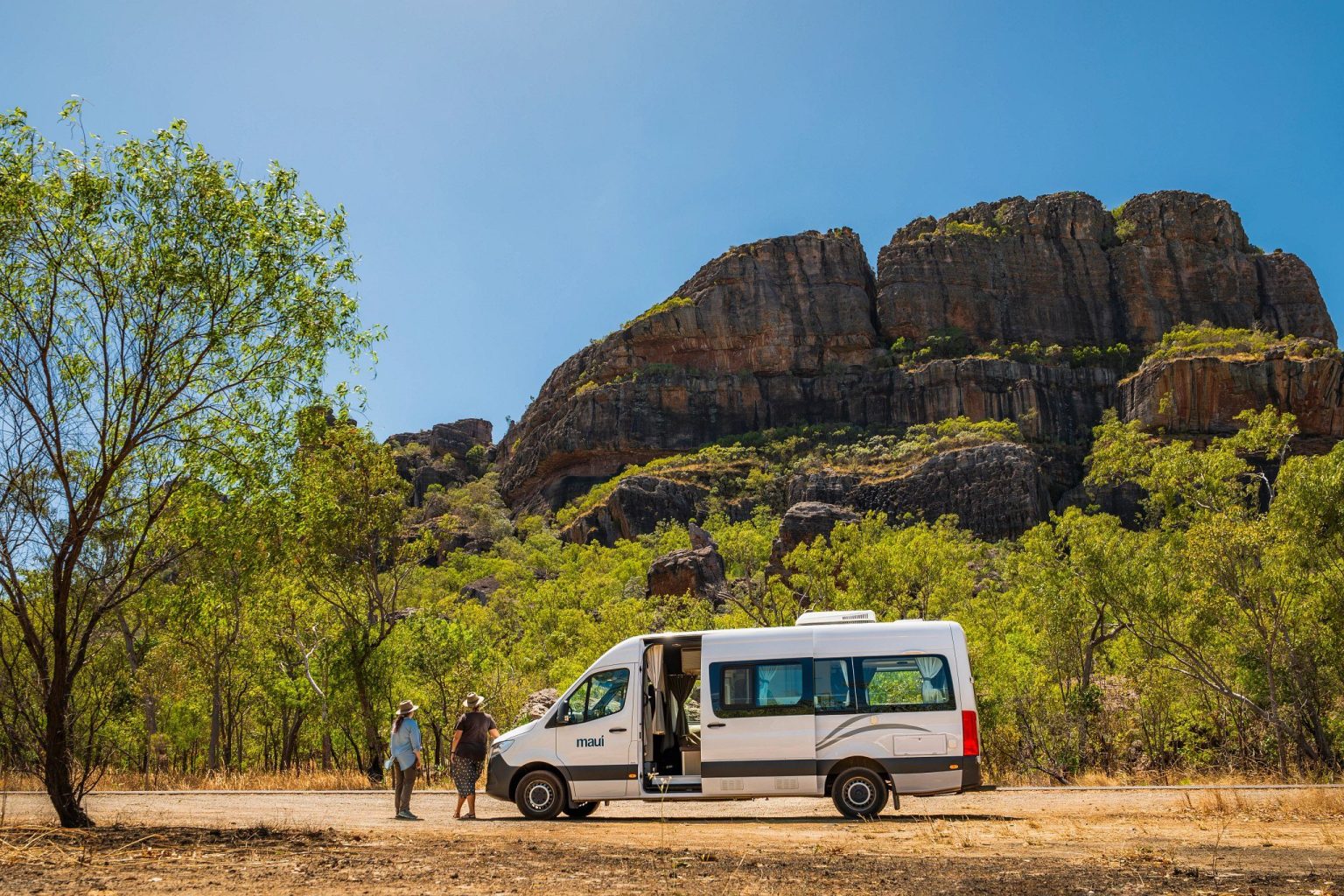Couple standing beside a campervan below a sandstone escarpment, Kakadu National Park, the Northern Territory