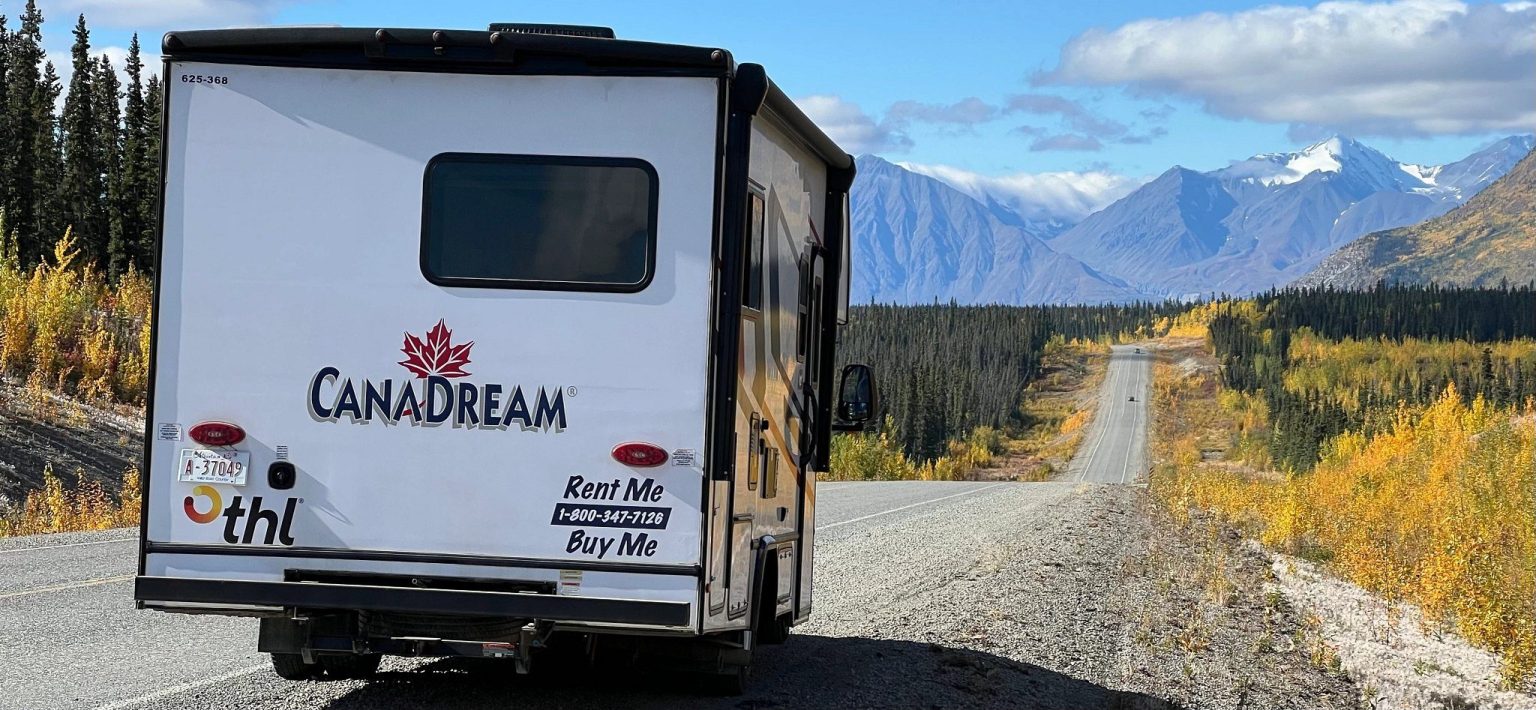 Rear of a motorhome on a gravel road through autumn hills, Yukon, Canada