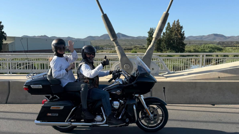 Rider and passenger waving from a Harley-Davidson on a South African bridge