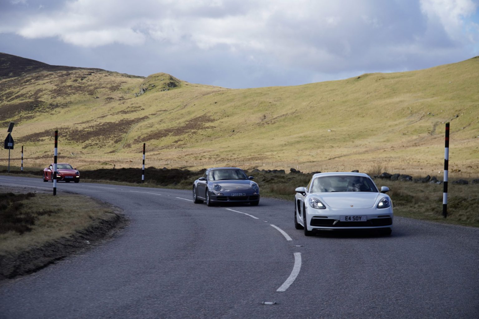 Porsches rounding a bend on a Highland road
