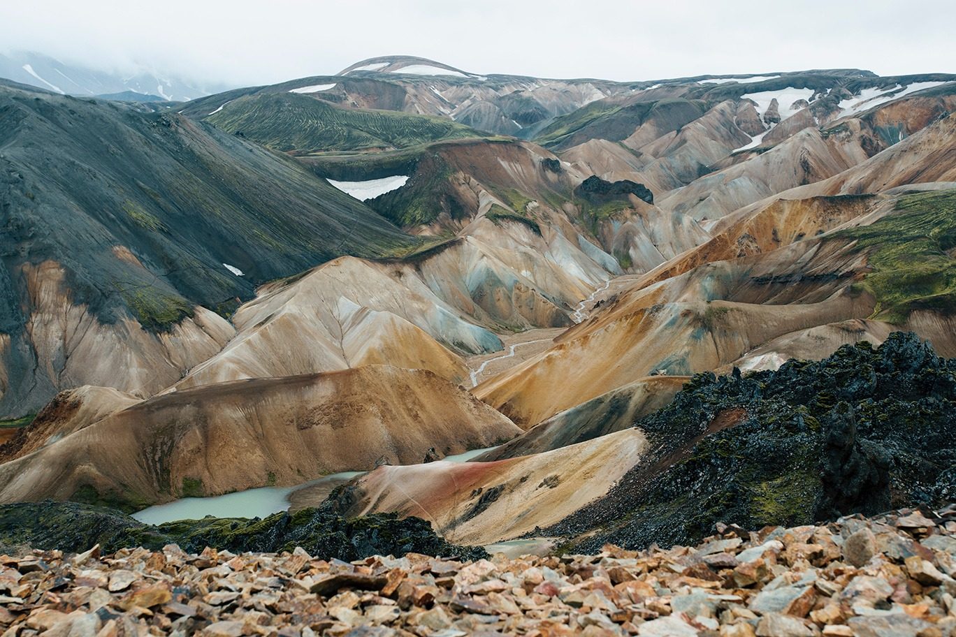 Colourful rhyolite hills with a small lake and black lava field in Iceland