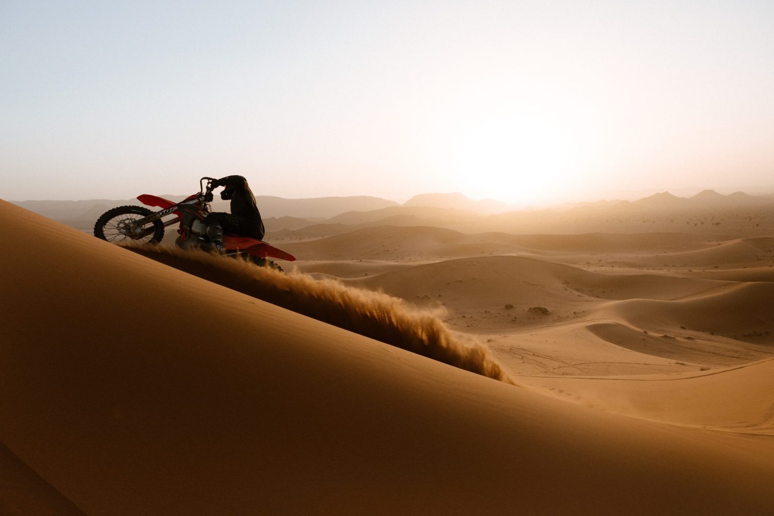 Motorcyclist riding across the Sahara dunes at golden hour