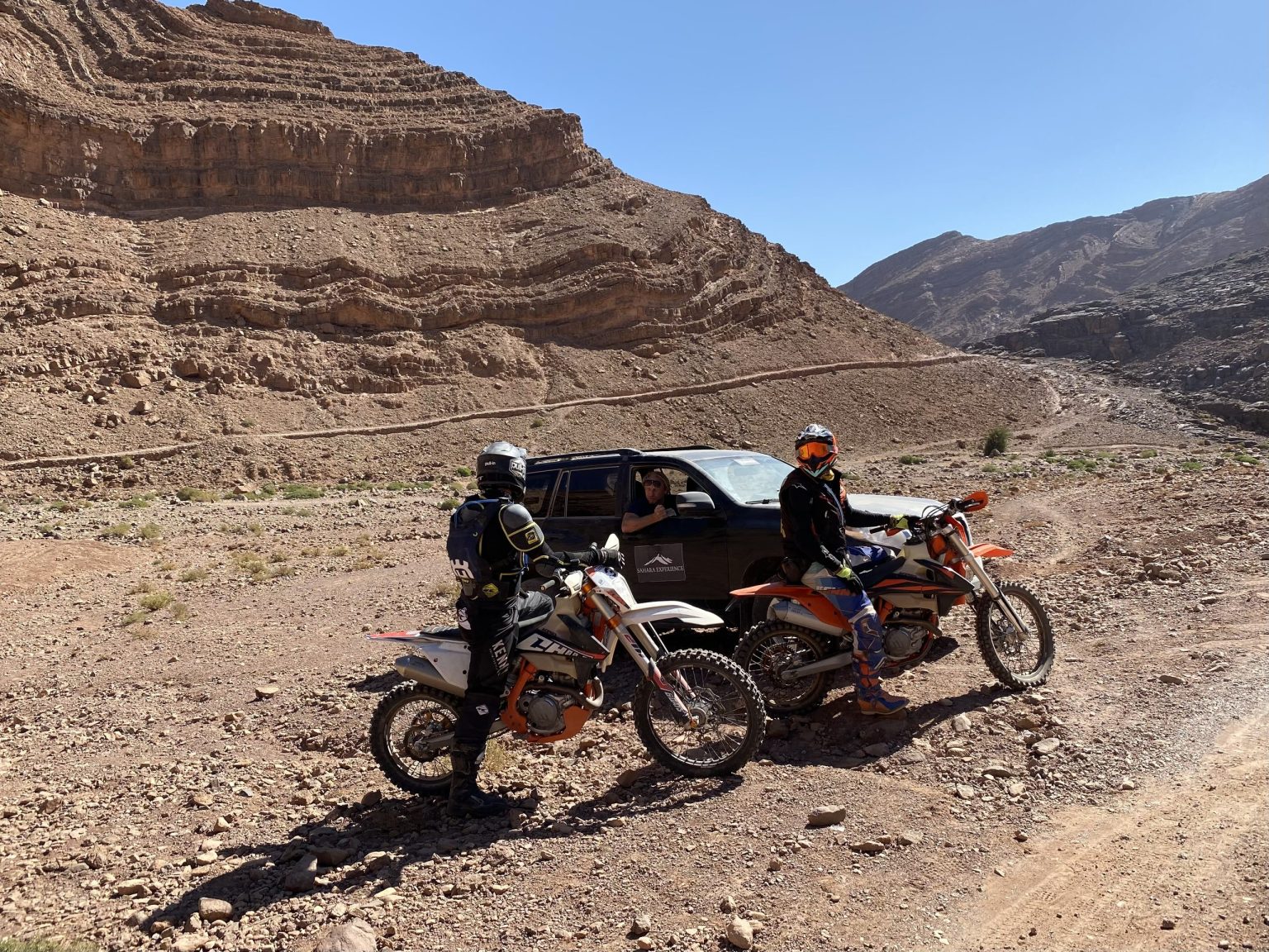Riders resting beside their dirt bikes in a High Atlas valley