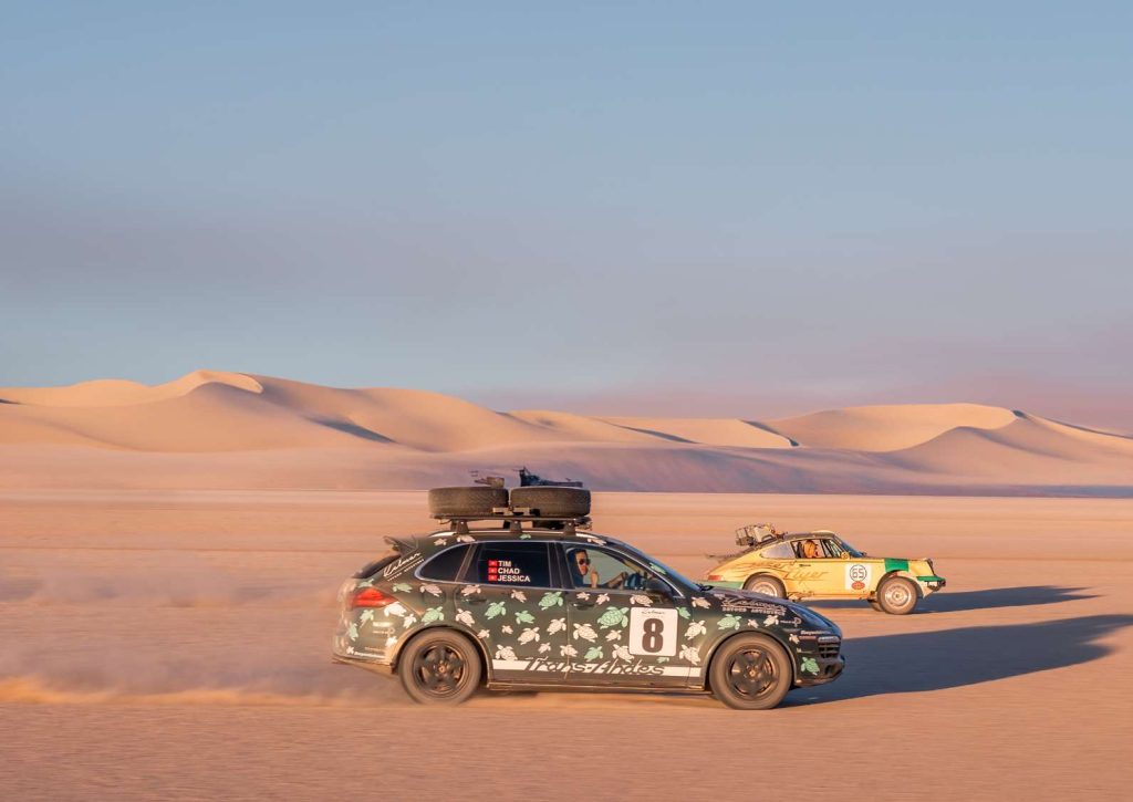 Two safari-prepared cars crossing the dunes at sunset in Namibia