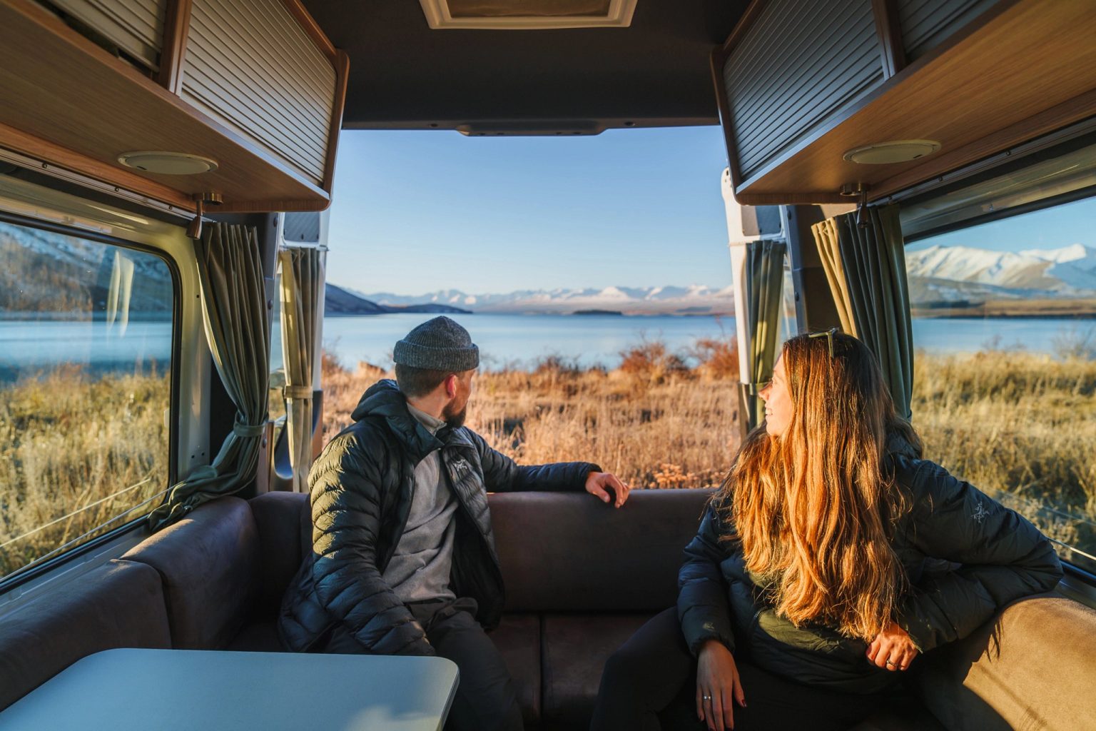 Couple sitting in the campervan lounge looking out at a lake, Lake Tekapo, New Zealand's South Island