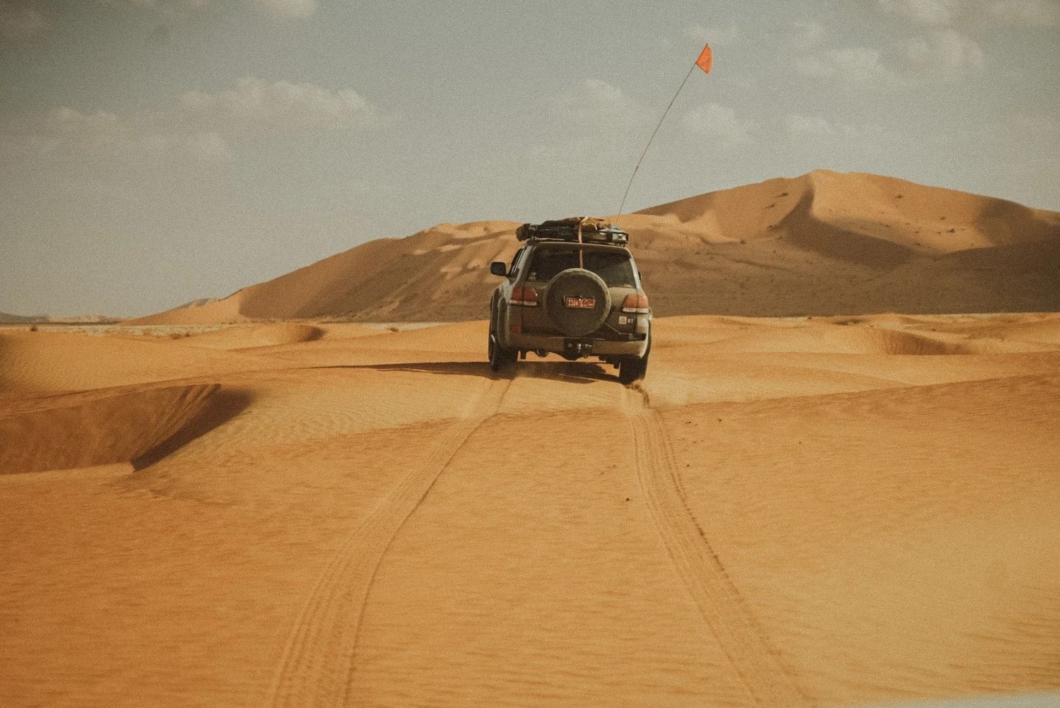 Four-wheel drive vehicle with orange flag crossing golden sand dunes in the Omani desert