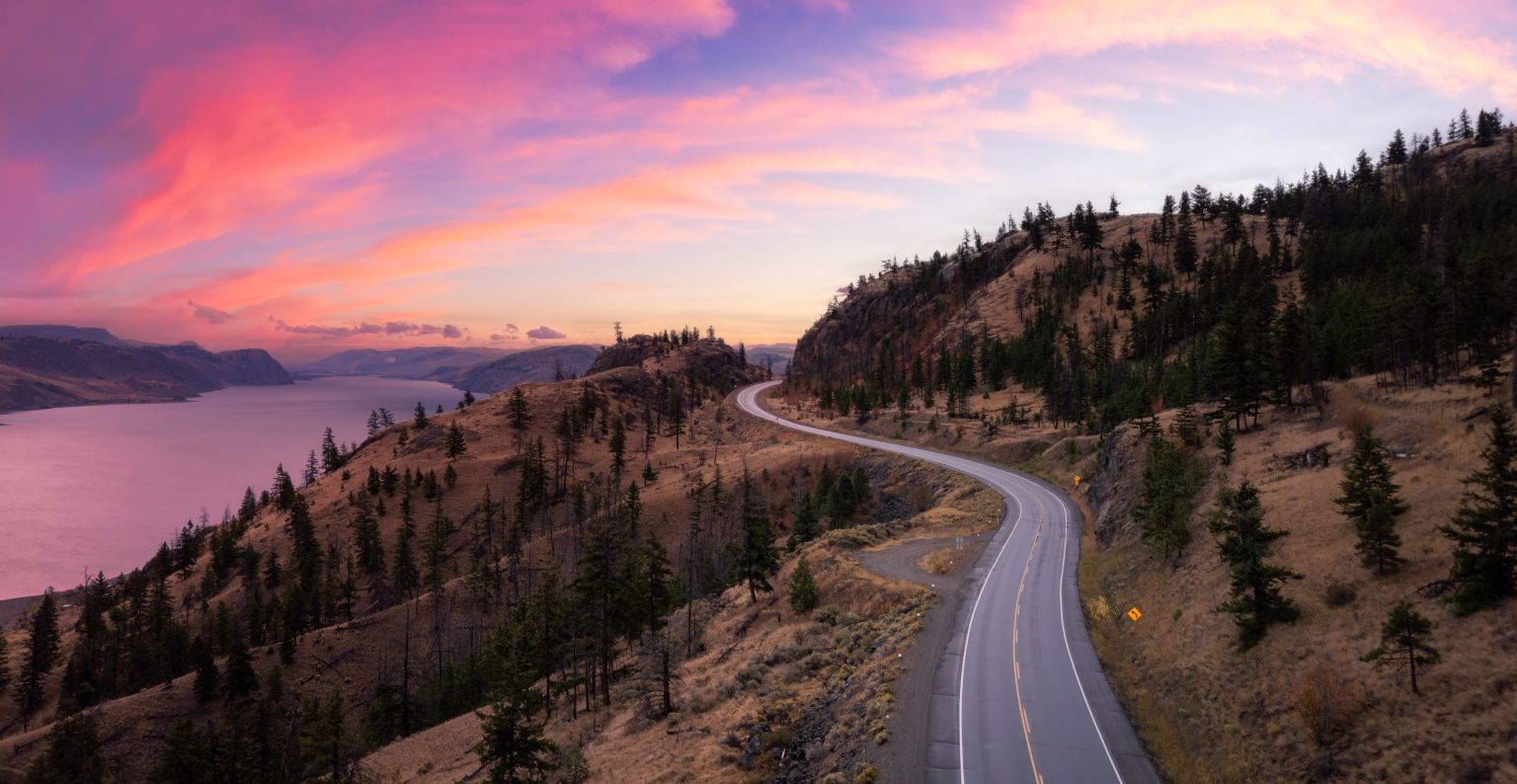 Winding road through dry hills above Okanagan Lake at sunset
