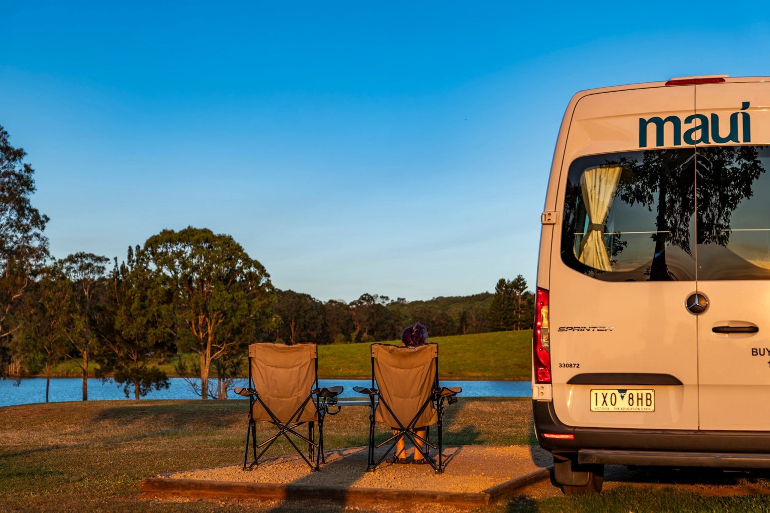 Two camp chairs beside a campervan overlooking a lake at sunset, Lake Tinaroo, Queensland