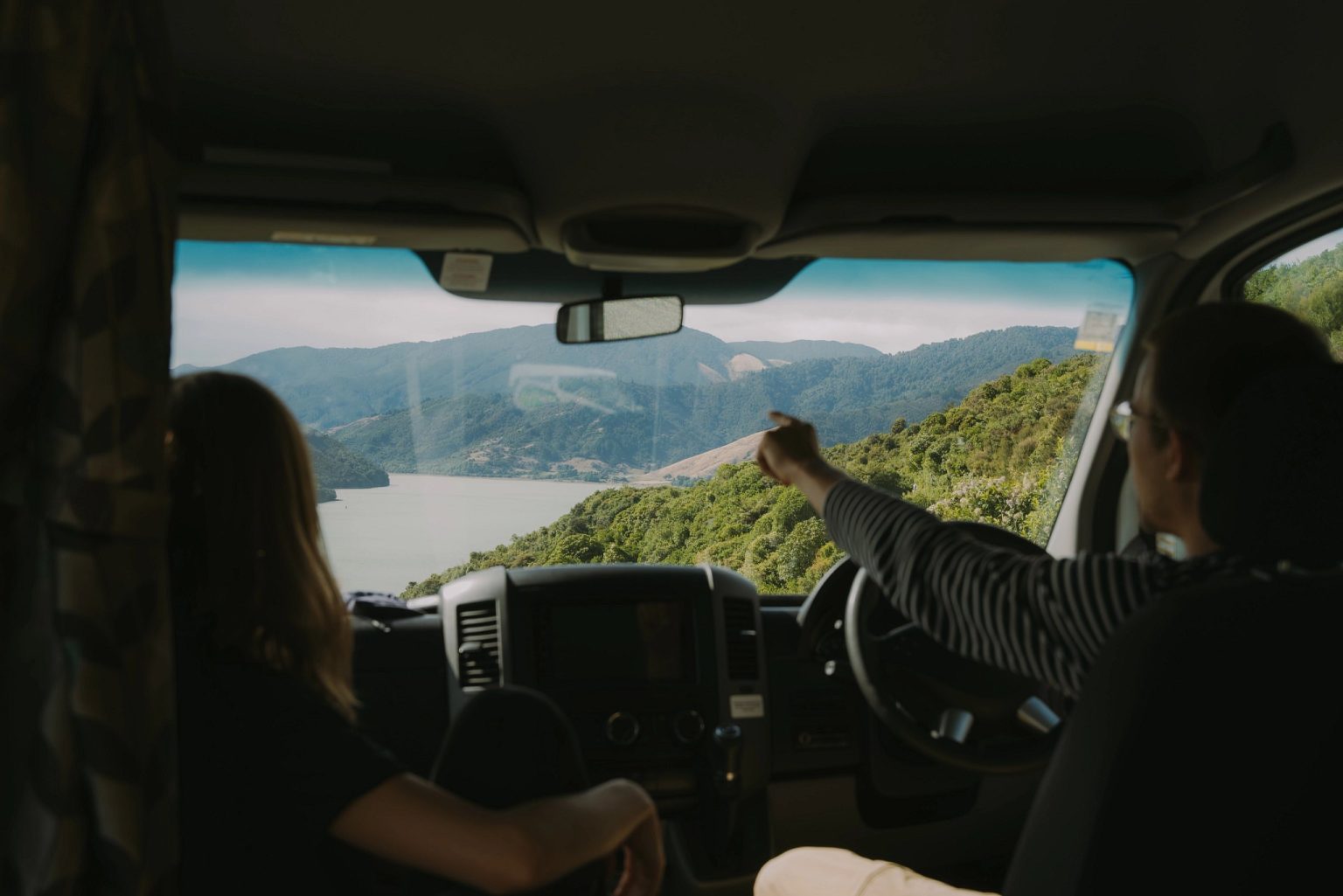 Couple in a campervan cab looking out at a lake and hills, Nelson, New Zealand's South Island