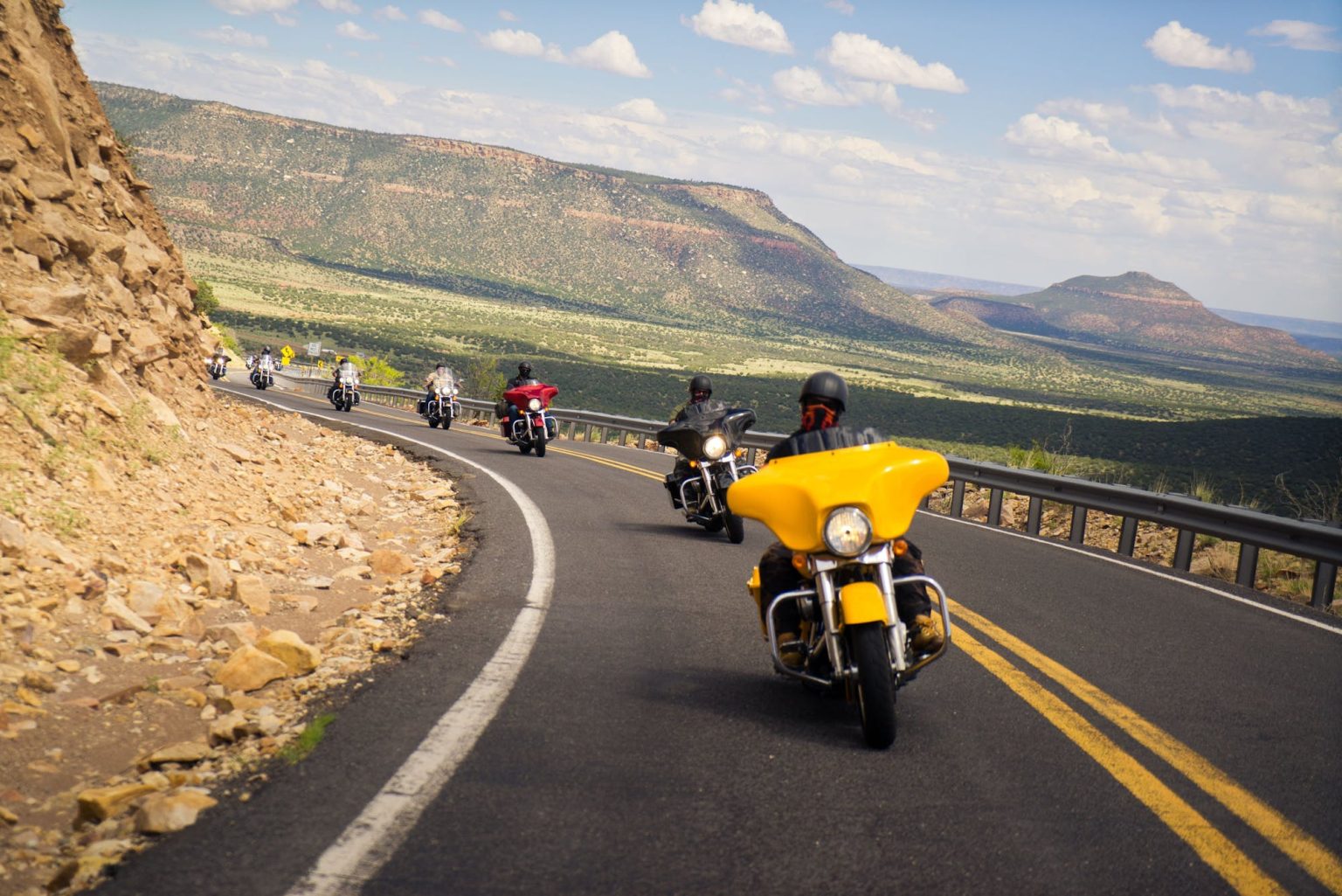 Group of riders on Harley-Davidsons on a winding mountain road above a valley