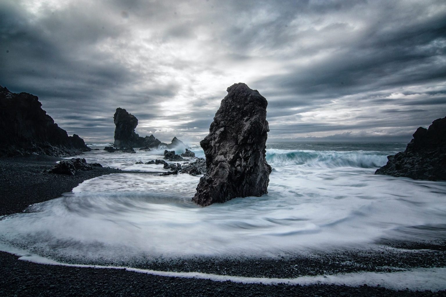 Black sea stack and foaming waves on a dark sand beach in Iceland