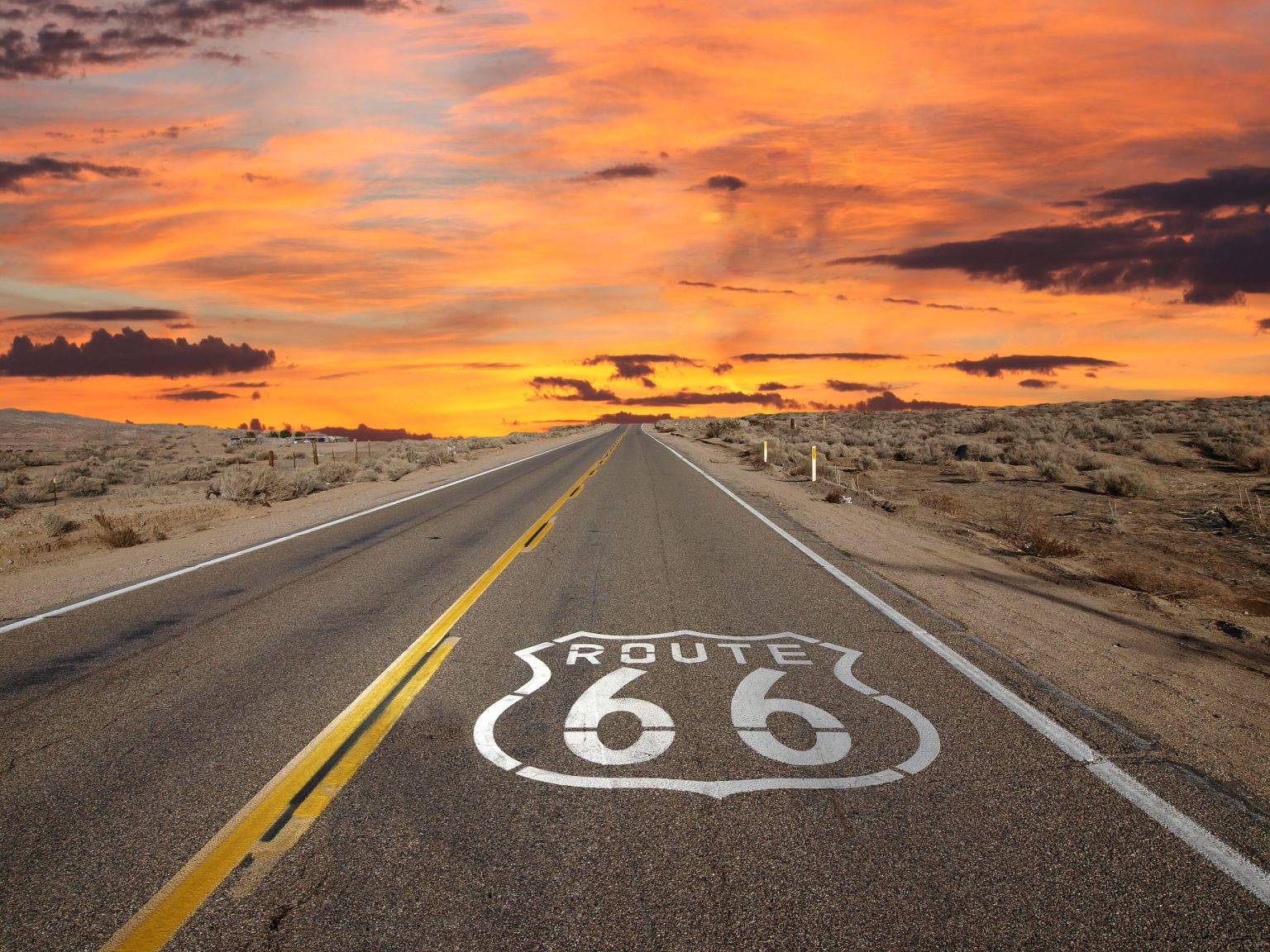Route 66 shield painted on an empty desert highway at sunset in the Mojave