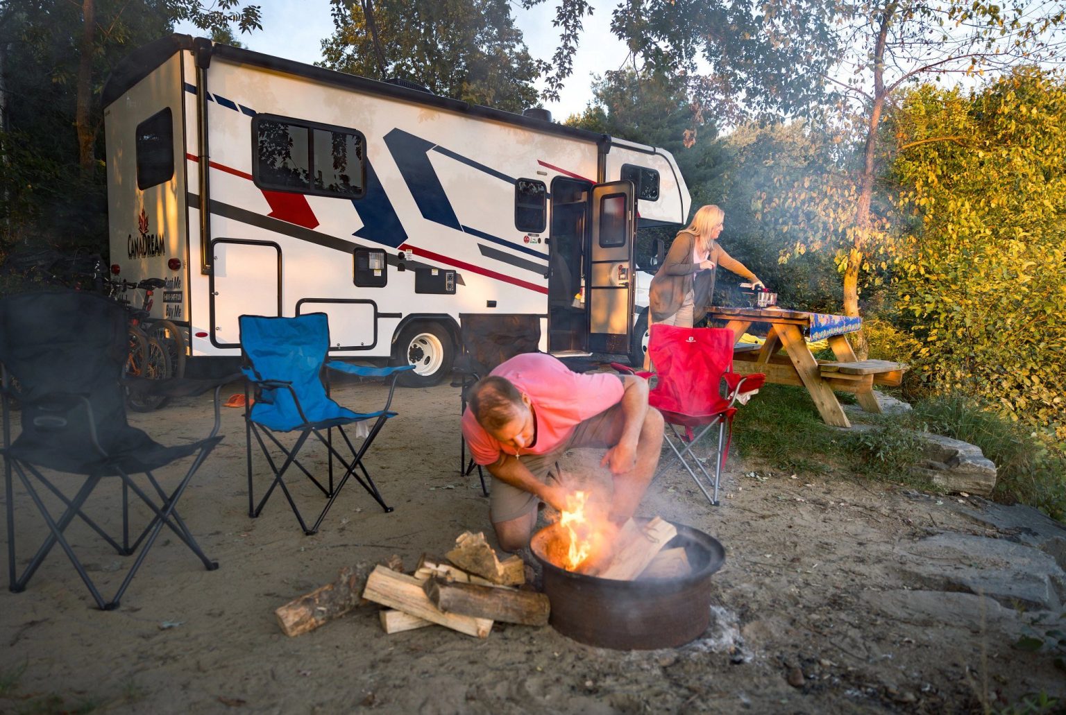 Couple lighting a fire pit beside a motorhome at camp, Ontario, Canada