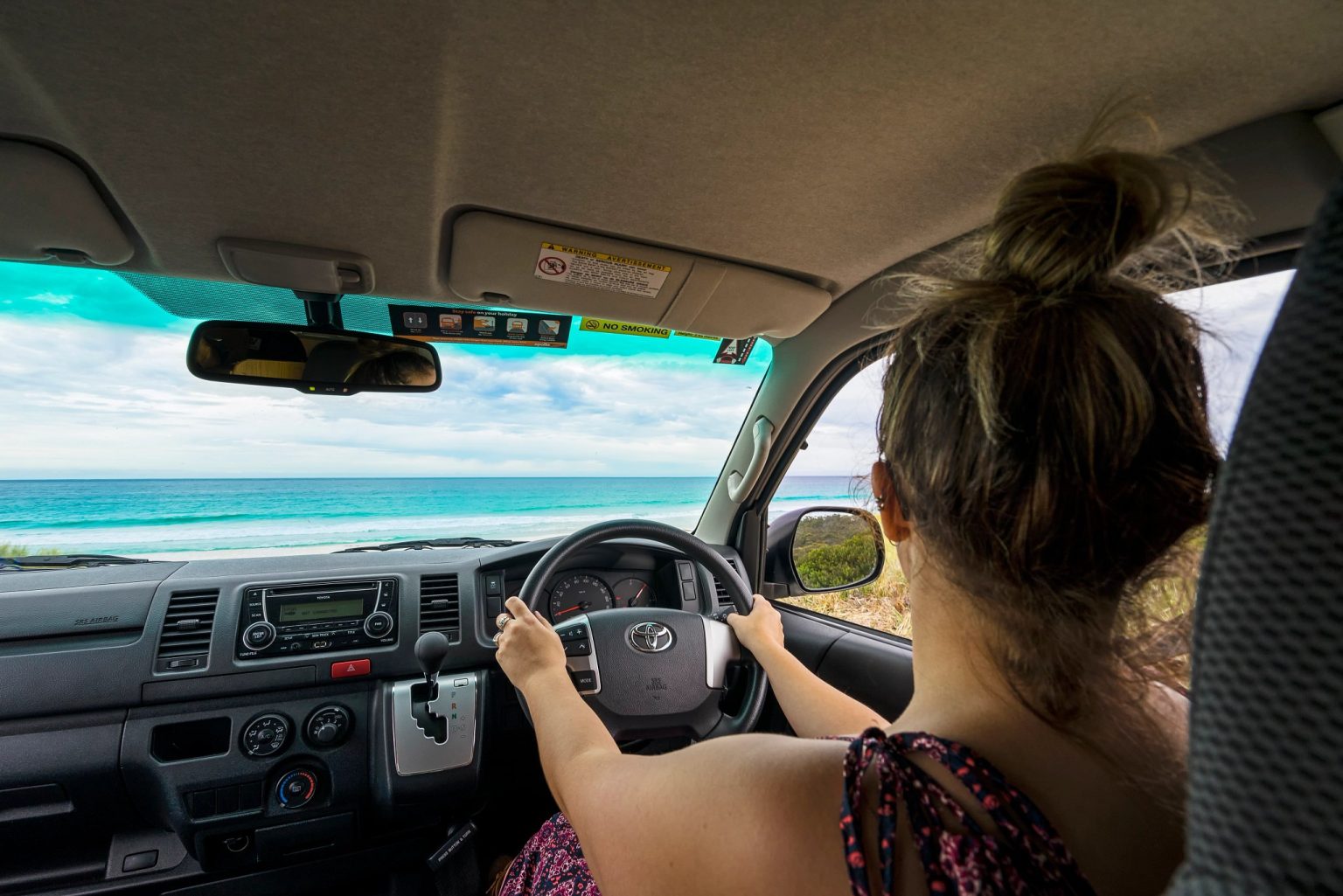 Woman driving a campervan along a coastal road, Tasmania
