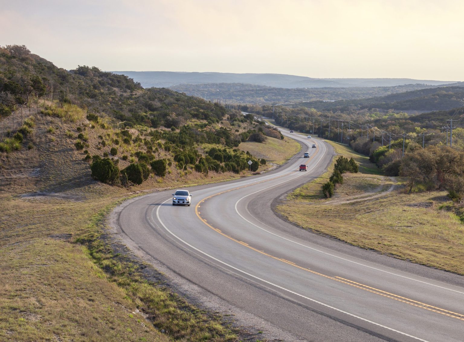 Highway curving through the rolling scrub of Texas Hill Country