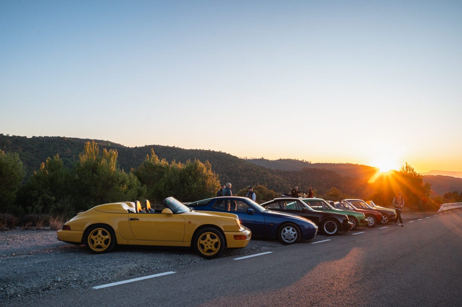 Classic Porsches parked on a mountain road at sunset in Catalonia