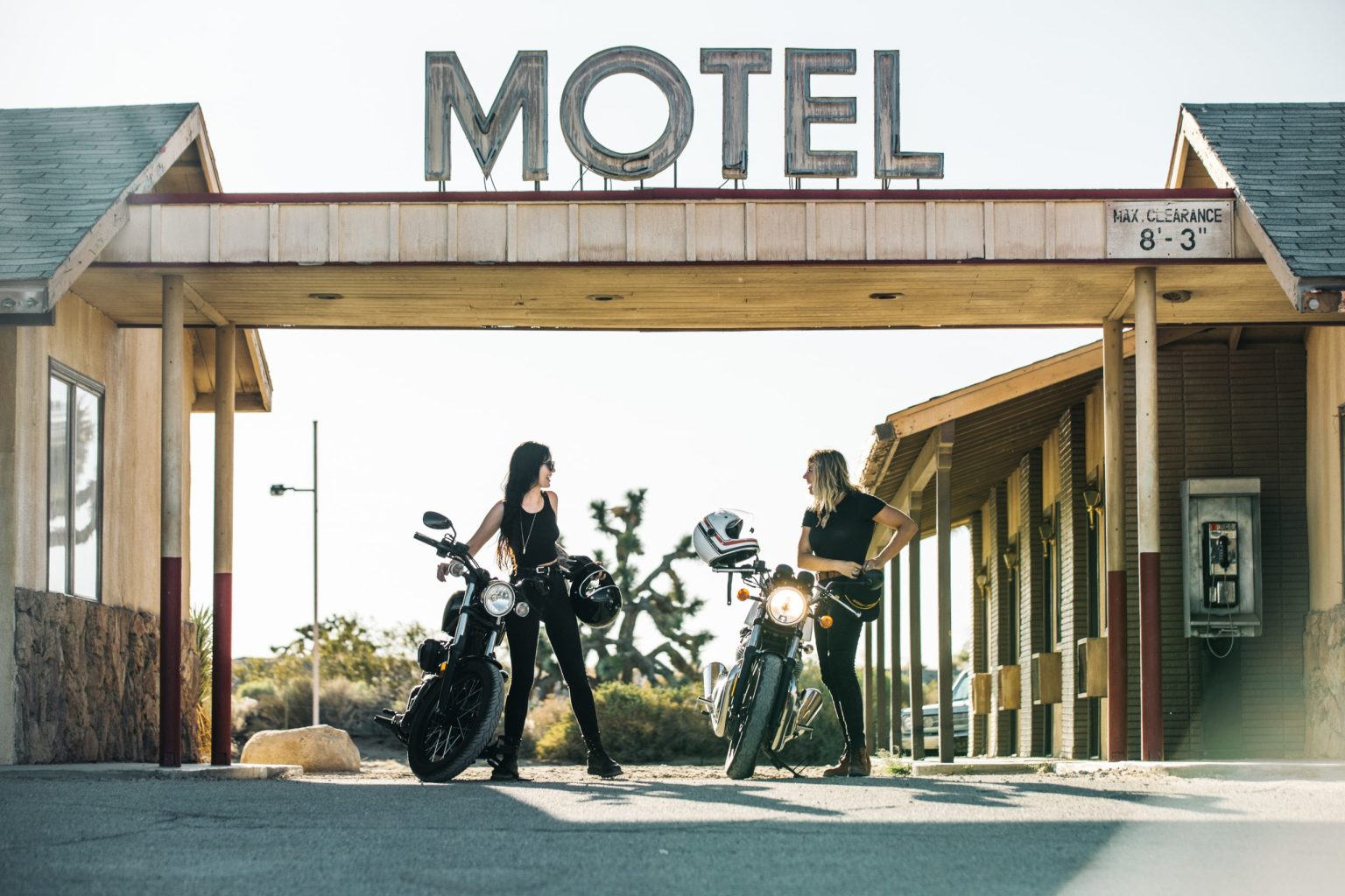 Two riders with motorcycles under a vintage motel sign