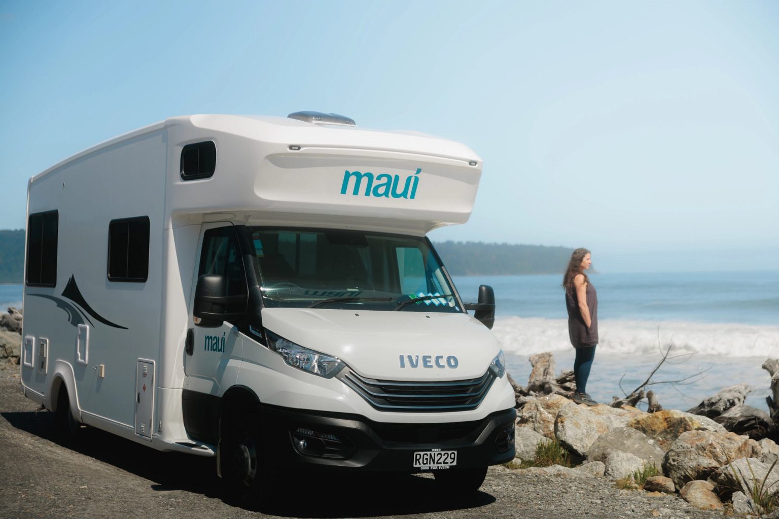 Motorhome parked on a rocky shoreline with a woman by the sea, West Coast, New Zealand's South Island