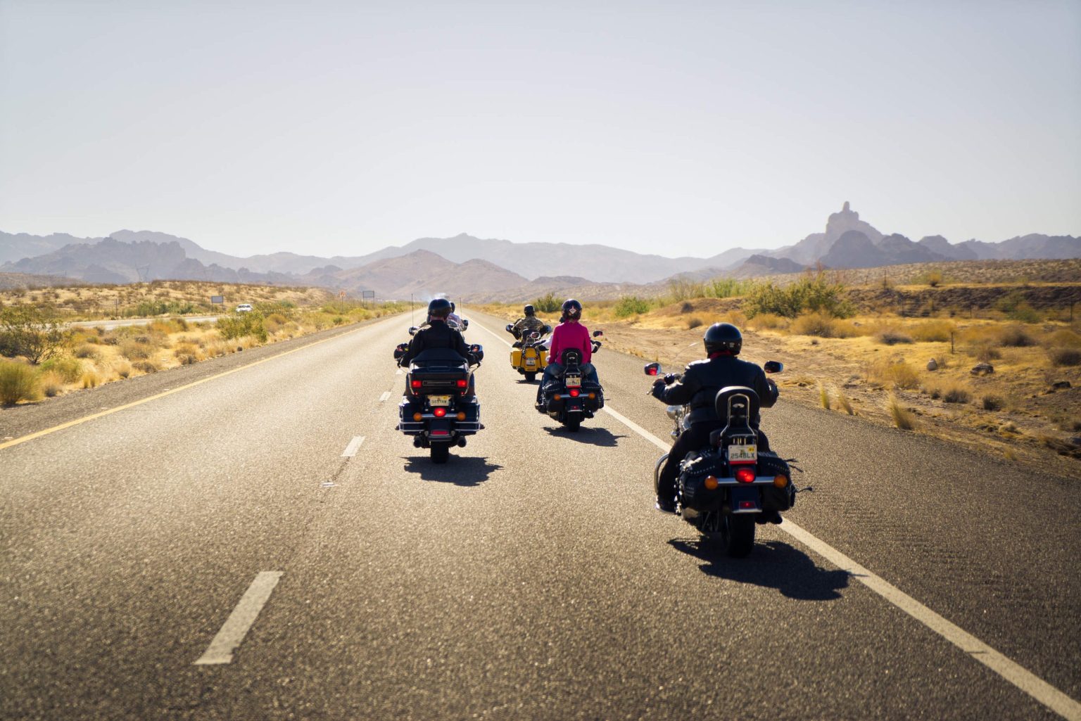 Three motorcyclists riding a desert highway toward distant mountains